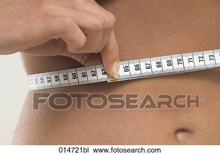 Stock Image - close-up of young women controlling her waistline with tape measure. Fotosearch
