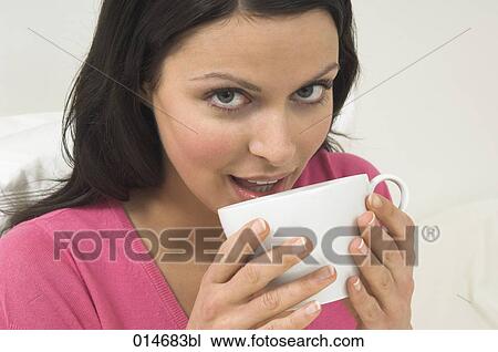 Stock Image - headshot of young woman drinking from white cup. Fotosearch