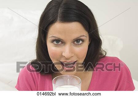 Stock Image - headshot of young woman drinking glass of milk. Fotosearch