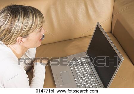 high angle view of young woman lying sofa with notebook computer and talking on cellphone View Large Photo Image Stock Image - high angle view of young woman lying sofa with notebook computer and talking on cellphone. Fotosearch