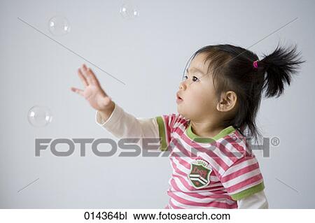 Stock Image - little girl trying to catch soap bubbles. Fotosearch