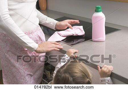 Stock Image - little girl watching her mother cleaning stove. Fotosearch