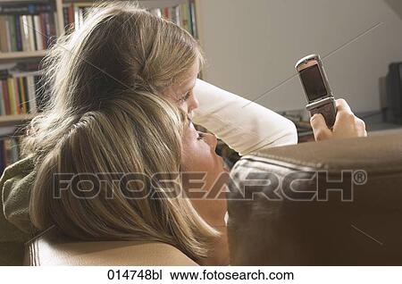 Stock Image - mother and little daughter lying on sofa together and looking at display of mobile phone. Fotosearch