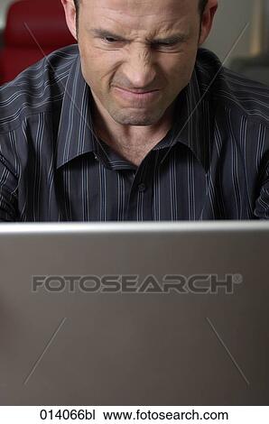 Stock Image - portrait of angry man looking frustrated at screen of laptop computer. Fotosearch