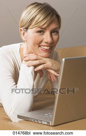 Stock Image - portrait of blonde woman on sofa with notebook computer. Fotosearch