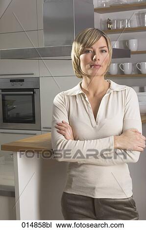 Stock Image - portrait of blonde young woman standing in kitchen. Fotosearch