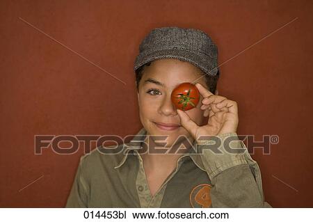 Stock Image - portrait of boy holding tomato before his eye. Fotosearch