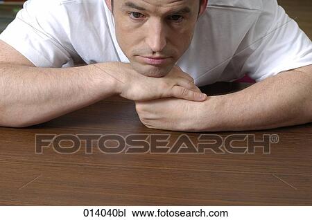 Stock Image - portrait of depressed man sitting at table. Fotosearch
