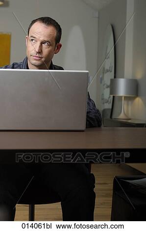 Stock Image - portrait of man sitting in living room working with notebook computer. Fotosearch