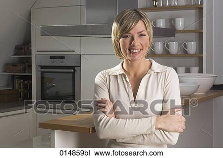 Stock Image - portrait of smiling young woman standing in kitchen. Fotosearch