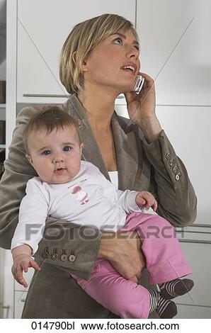 Stock Image - portrait of young businesswoman holding baby while talking on mobile phone. Fotosearch