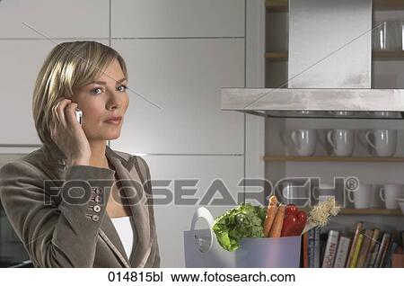 Stock Image - portrait of young businesswoman standing in kitchan and talking on mobile phone. Fotosearch