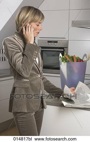 portrait of young businesswoman standing in kitchen, talking on mobile phone and reading newspaper View Large Photo Image Stock Image - portrait of young businesswoman standing in kitchen, talking on mobile phone and reading newspaper. Fotosearch