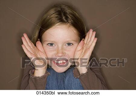 Stock Image - portrait of young girl peeking between her hands. Fotosearch