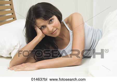 Stock Image - portrait of young woman lying in bed looking at camera. Fotosearch