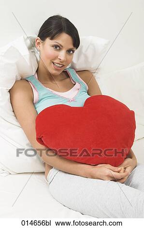 portrait of young woman lying in bed holding red cushion in shape of heart View Large Photo Image Stock Image - portrait of young woman lying in bed holding red cushion in shape of heart. Fotosearch