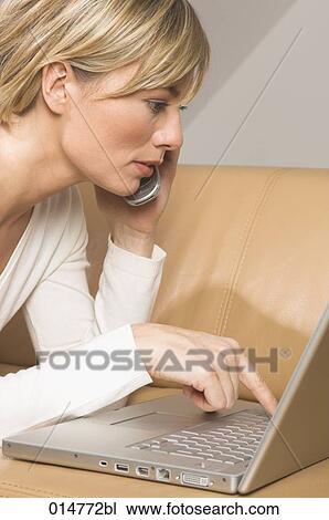 portrait of young woman lying on sofa typing on notebook computer and listening to mobile phone View Large Photo Image Stock Image - portrait of young woman lying on sofa typing on notebook computer and listening to mobile phone. Fotosearch