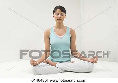 Stock Image - portrait of young woman sitting on bed doing yog in lotus position. Fotosearch