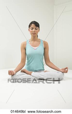 Stock Image - portrait of young woman sitting on bed doing yog in lotus position. Fotosearch