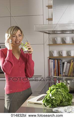 Stock Image - portrait of young woman with cellphone, drinking glass of milk in kitchen. Fotosearch
