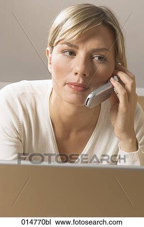 Stock Image - portrait of young woman with notebook computer talking on cellphone. Fotosearch