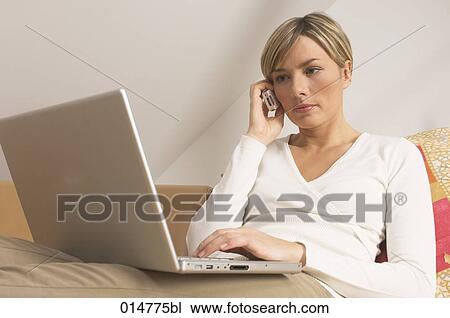 Stock Image - portrait of young woman working with laptop computer and talking on mobile phone. Fotosearch