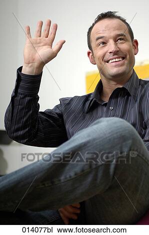 smiling young man sitting and raising hand View Large Photo Image Stock Image - smiling young man sitting and raising hand. Fotosearch