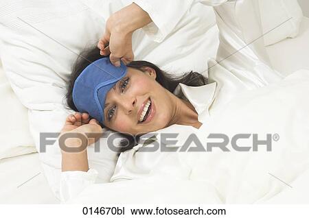 Stock Image - smiling young woman wearing sleep mask waking up in the morning. Fotosearch
