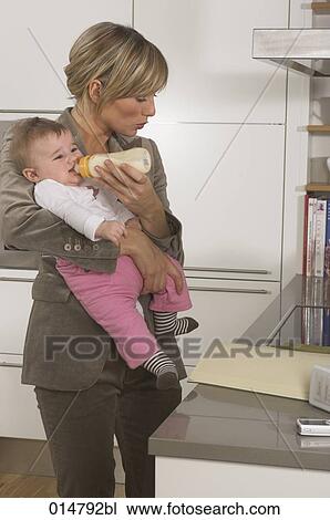 Stock Image - young businesswoman feeding her baby while reading documents. Fotosearch