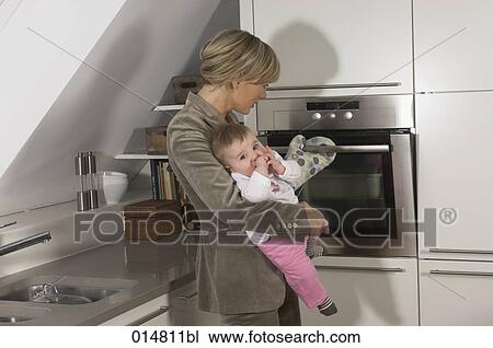 young businesswoman holding her baby while standing at the oven View Large Photo Image Stock Image - young businesswoman holding her baby while standing at the oven. Fotosearch