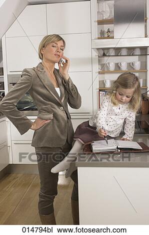 young businesswoman standing in kitchen and talking on cellphone while daughter is playing with her journal View Large Photo Image Stock Image - young businesswoman standing in kitchen and talking on cellphone while daughter is playing with her journal. Fotosearch