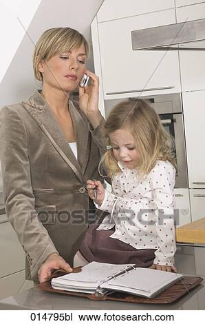 young businesswoman standing in kitchen and talking on cellphone while daughter is playing with her journal View Large Photo Image Stock Image - young businesswoman standing in kitchen and talking on cellphone while daughter is playing with her journal. Fotosearch