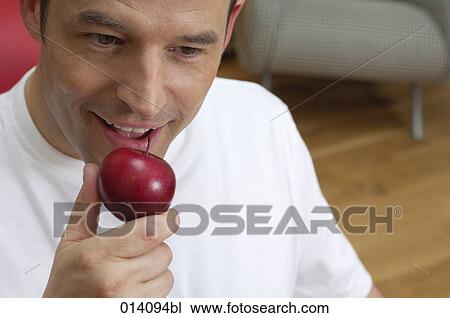 Stock Image - young man tasting red apple. Fotosearch