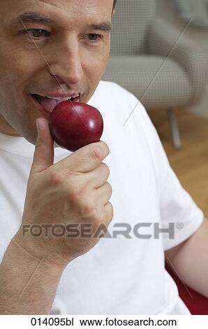 Stock Image - young man tasting red apple. Fotosearch