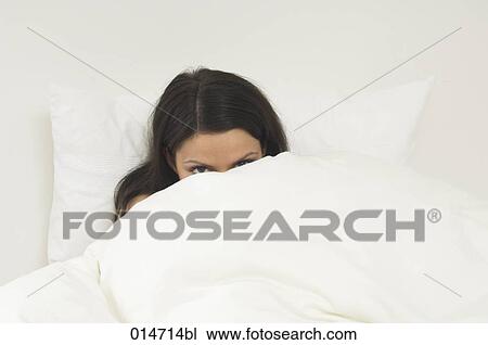 Stock Image - young woman hiding in bed behind duvet. Fotosearch