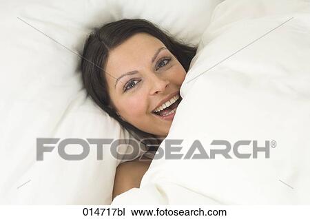 Stock Image - young woman hiding in bed behind duvet. Fotosearch