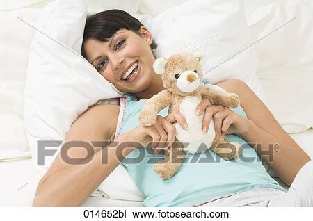 young woman lying in bed holding little teddy bear View Large Photo Image Stock Image - young woman lying in bed holding little teddy bear. Fotosearch