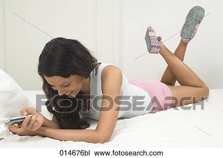 young woman lying on bed laughing and holding mobile phone View Large Photo Image Stock Image - young woman lying on bed laughing and holding mobile phone. Fotosearch