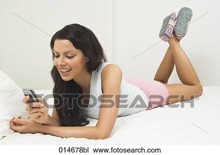 young woman lying on bed writing text messages in mobile View Large Photo Image Stock Image - young woman lying on bed writing text messages in mobile. Fotosearch