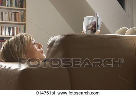 young woman lying on leather sofa reading magazine View Large Photo Image Stock Image - young woman lying on leather sofa reading magazine. Fotosearch