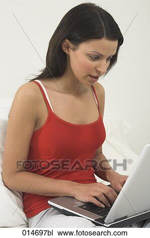 Stock Image - young woman sitting in bed with laptop computer. Fotosearch