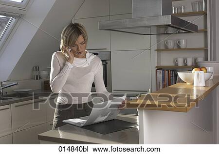 young woman standing in kitchen talking on cellphone and looking at file View Large Photo Image Stock Image - young woman standing in kitchen talking on cellphone and looking at file. Fotosearch