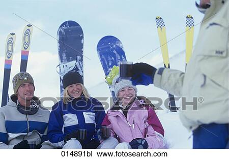 Stock Image - group of four friends sitting in snow drinking mulled wine. Fotosearch