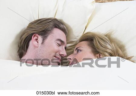 Stock Image - headshot of young couple in bed woman tenderly looking at sleeping man. Fotosearch