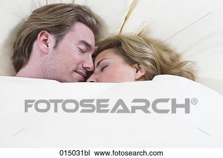 Stock Image - headshot of young couple sleeping closely together in bed. Fotosearch