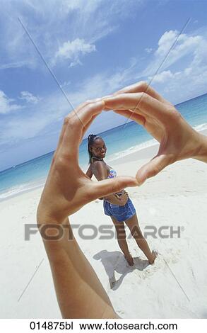 Stock Image - portait of woman on beach with hands forming frame in foreground. Fotosearch