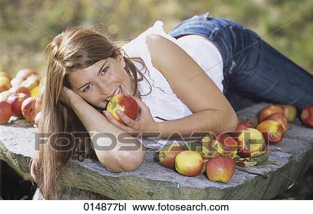Stock Image - portrait of long haired young woman eating apples. Fotosearch
