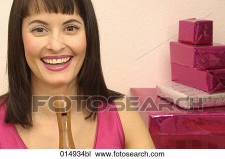 Stock Image - portrait of smiling young woman holding recorder with christmas presents in background. Fotosearch