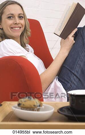 woman sitting on armchair reading booking with muffin and cup on tray in foreground View Large Photo Image Stock Image - woman sitting on armchair reading booking with muffin and cup on tray in foreground. Fotosearch