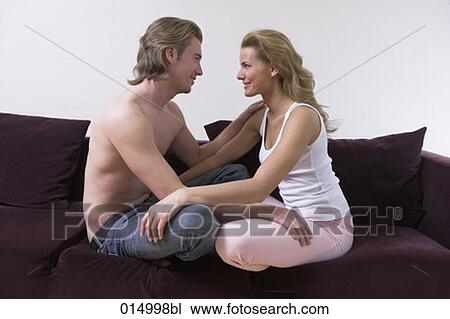 young couple sitting cross-legged on sofa tenderly looking at each other View Large Photo Image Stock Image - young couple sitting cross-legged on sofa tenderly looking at each other. Fotosearch